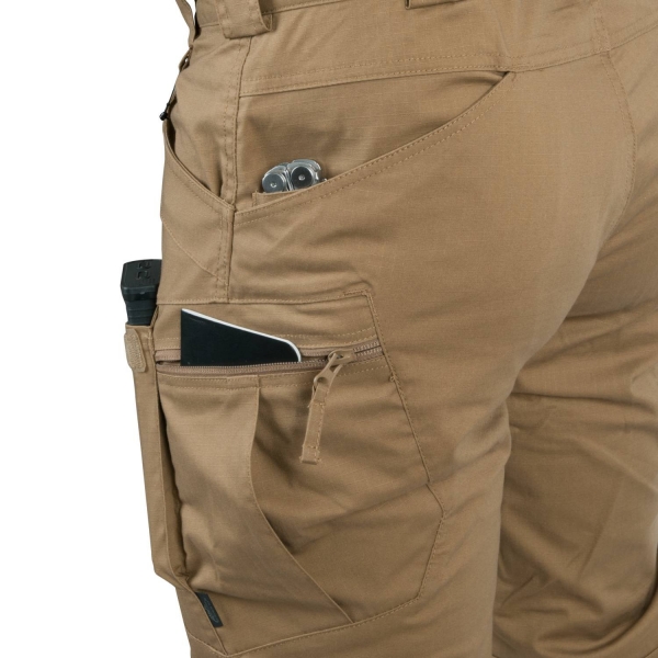 Eine lange braune Helikon Tex Hose von hinten links betrachtet. In drei verschiedenen Hosentaschen sind jeweils Gegenstände.