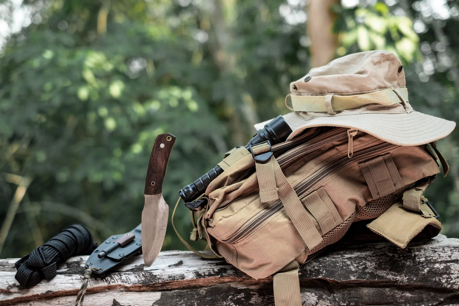 Ein Rucksack im Wald auf einem Baumstamm neben einen Messer und einem Seil.