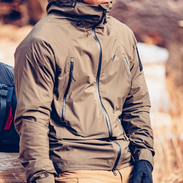 Die coyote farbene Softshell Jacke getragen von einem Mann der draußen ist und Handschuhe trägt.